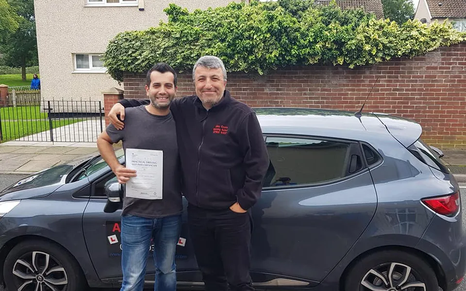 Alex Cross, in his driving school fleece, with a pupil who has just passed, beside the grey Renault Clio he teaches in